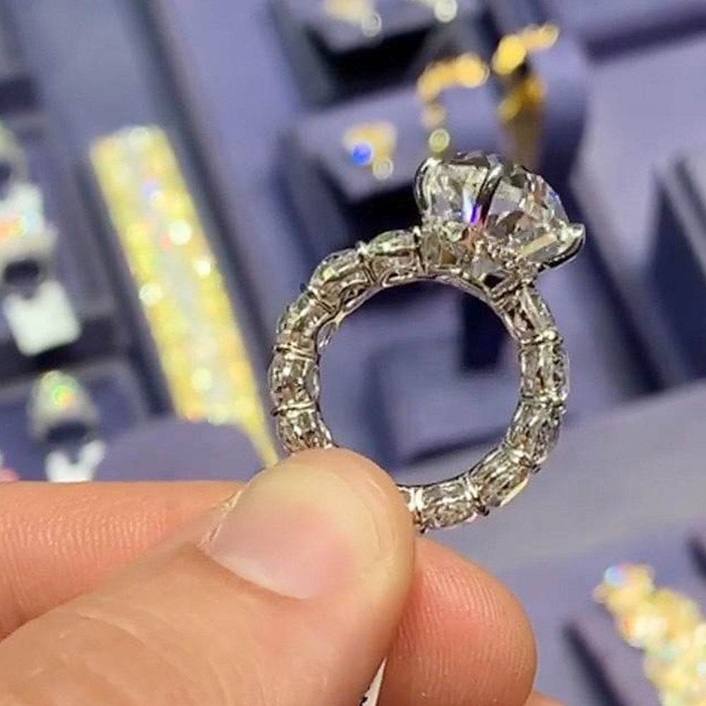 Close-up of horse eye-shaped zircon fashion ring ornament held between fingers with blurred jewelry display background