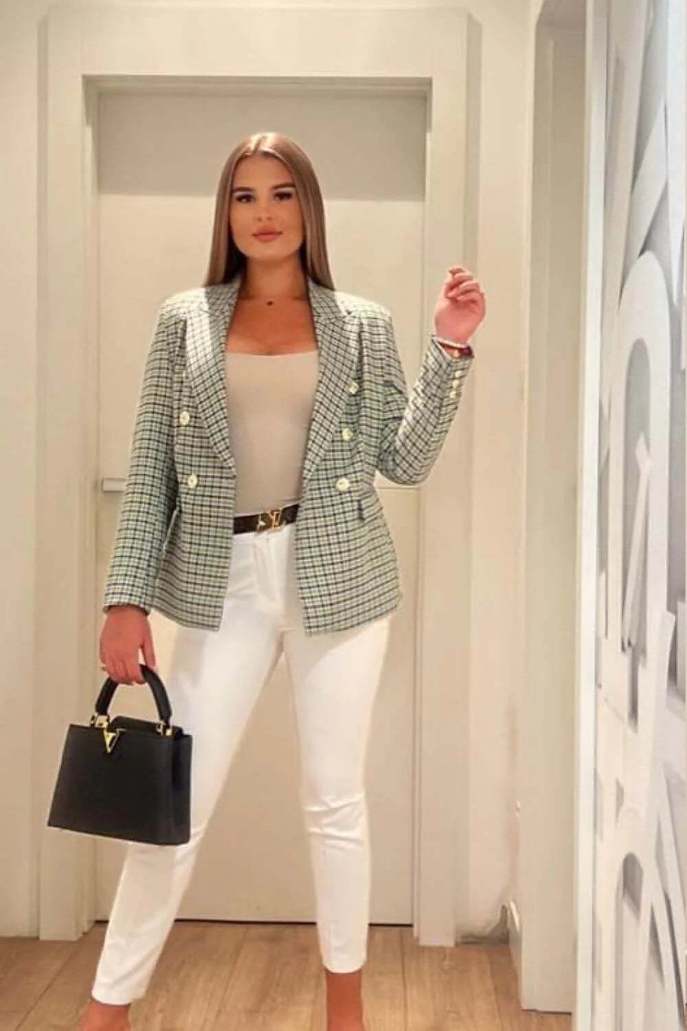 Stylish woman in a checked blazer, white pants, and a handbag, showcasing a chic business outfit suitable for any season.