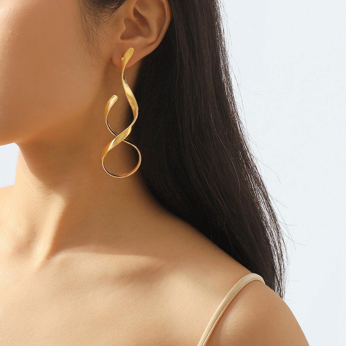 Asymmetric gold simple metal earrings with twisted design worn on ear