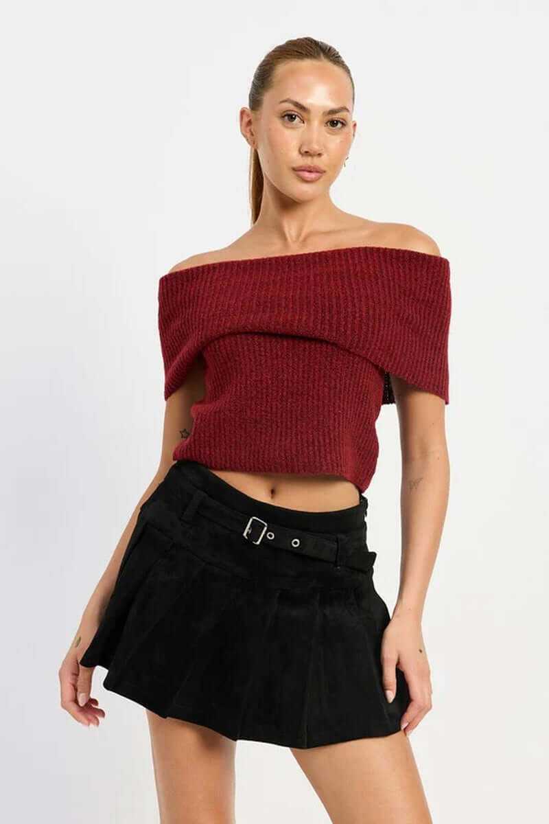 Model wearing a red off-shoulder knit top with a black pleated suede belted skort, showcasing a chic fall outfit.