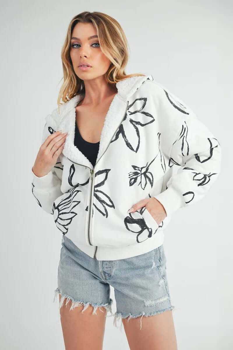 Model wearing Oita bomber jacket with floral design, hood, zip closure, and casual shorts, showcasing stylish comfort.