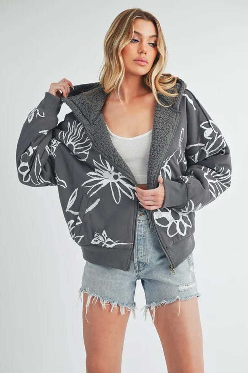 Woman wearing Oita jacket with floral design, oversized fit, and soft sherpa lining, styled with denim shorts.