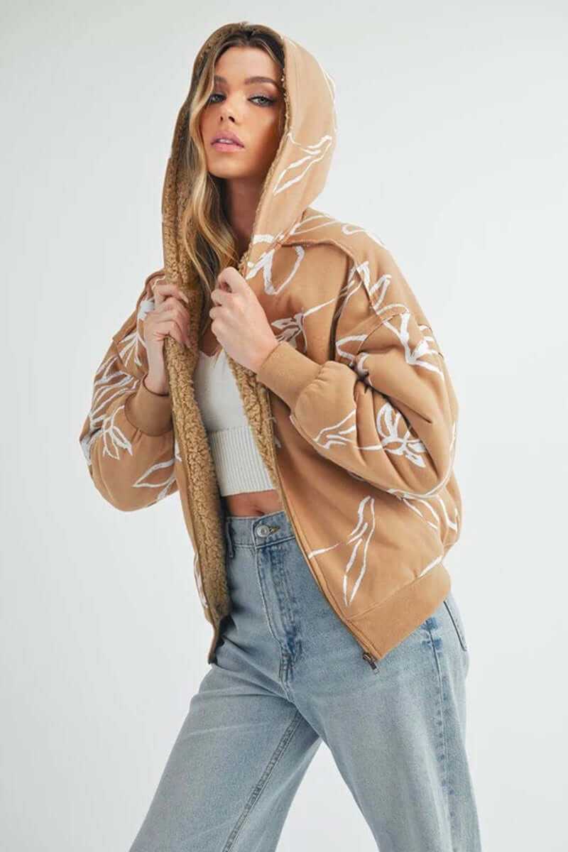 Model wearing Oita jacket with a hood, featuring floral prints and sherpa lining, styled with high-waisted jeans.