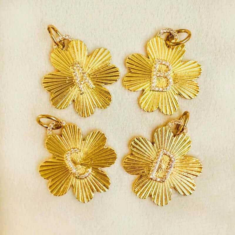 Four gold clover charms with initials A, B, C, and D, featuring a floral design and sparkly accents.