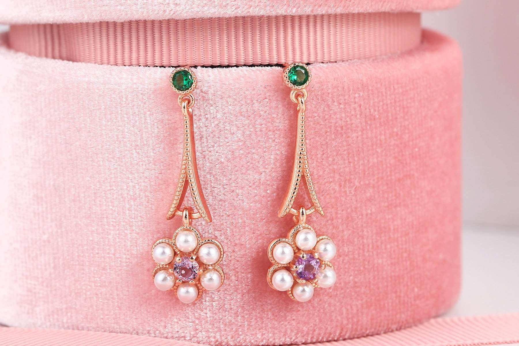 rose gold earrings with green gem studs and amethyst tassel flower pendants with pearls on pink velvet background