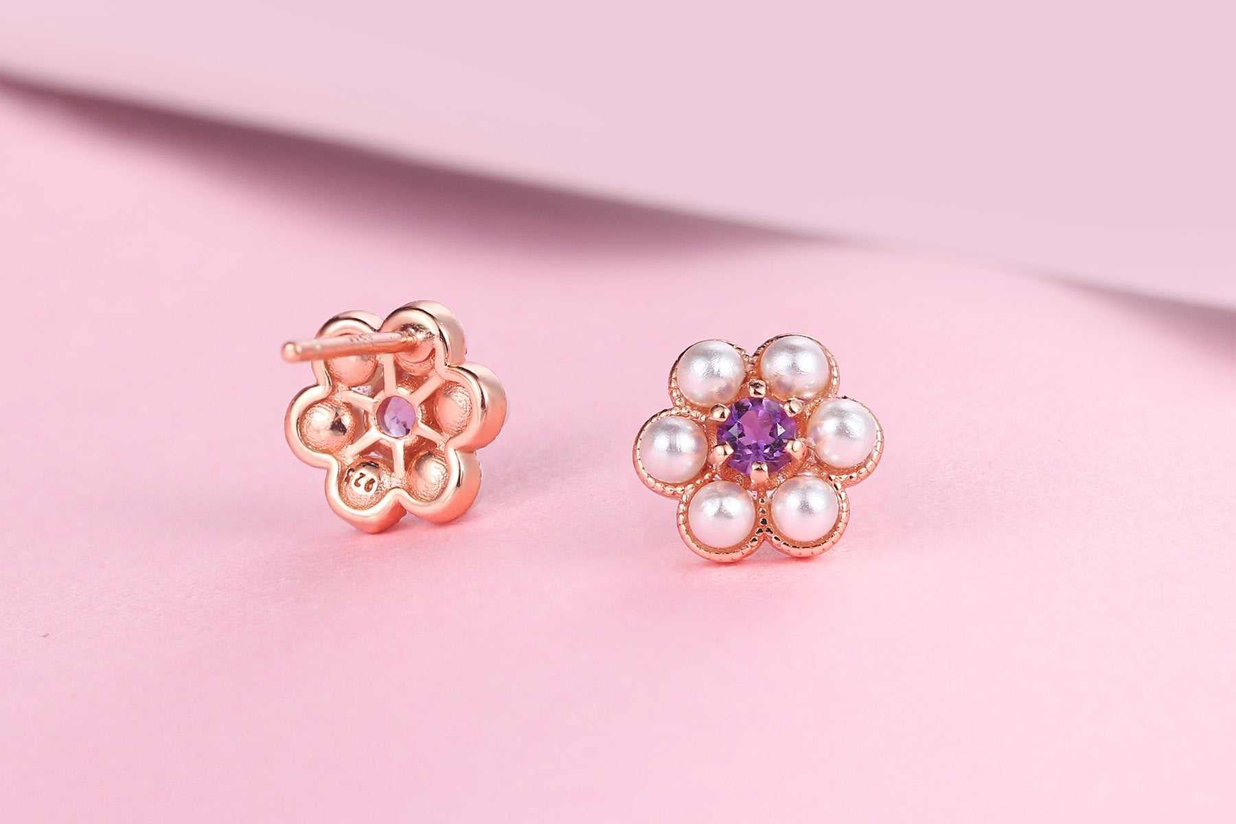 Rose gold plum blossom earrings with amethyst center and pearl accents on a pink background