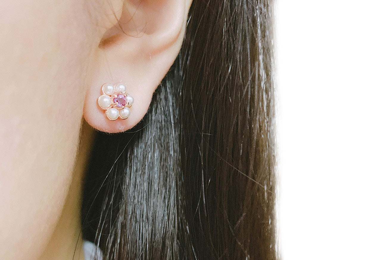 Close-up of a floral stud earring with pearl petals and a pink amethyst center on a woman's ear
