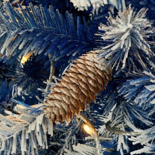 Close-up of blue pre-lit artificial Christmas tree branch with frosted pine cone and warm white LED lights