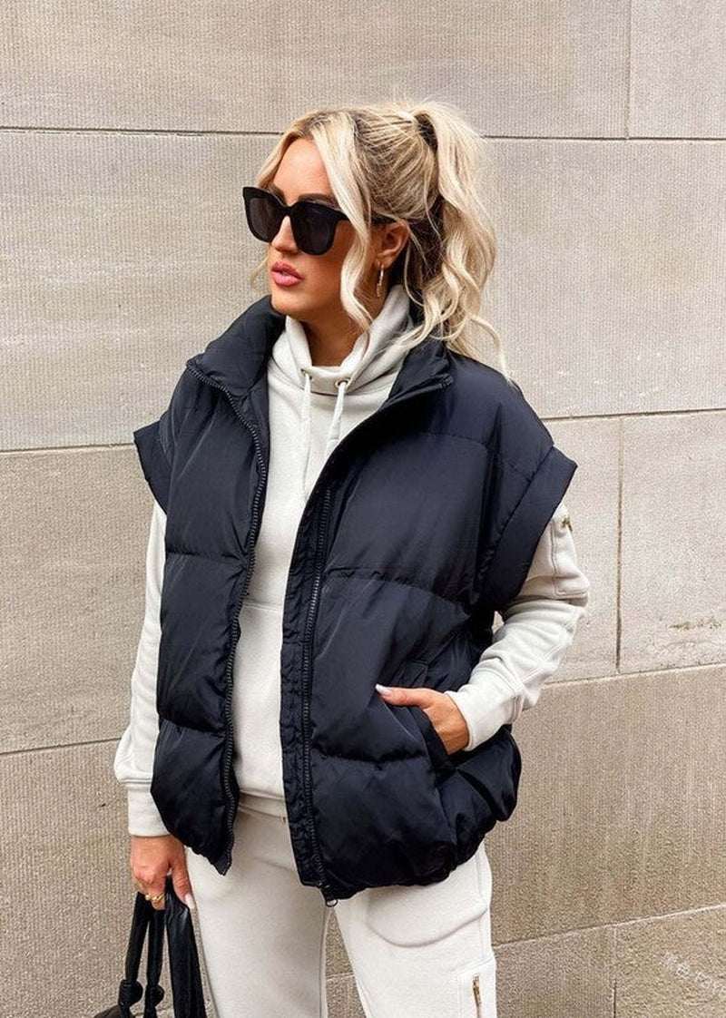 Stylish woman wearing a black puffer vest over a gray hoodie, showcasing modern winter fashion.