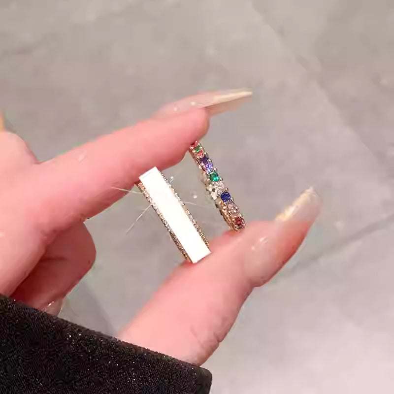 Close-up of a hand holding a rainbow gemstone ring and a white band ring with zircon stones
