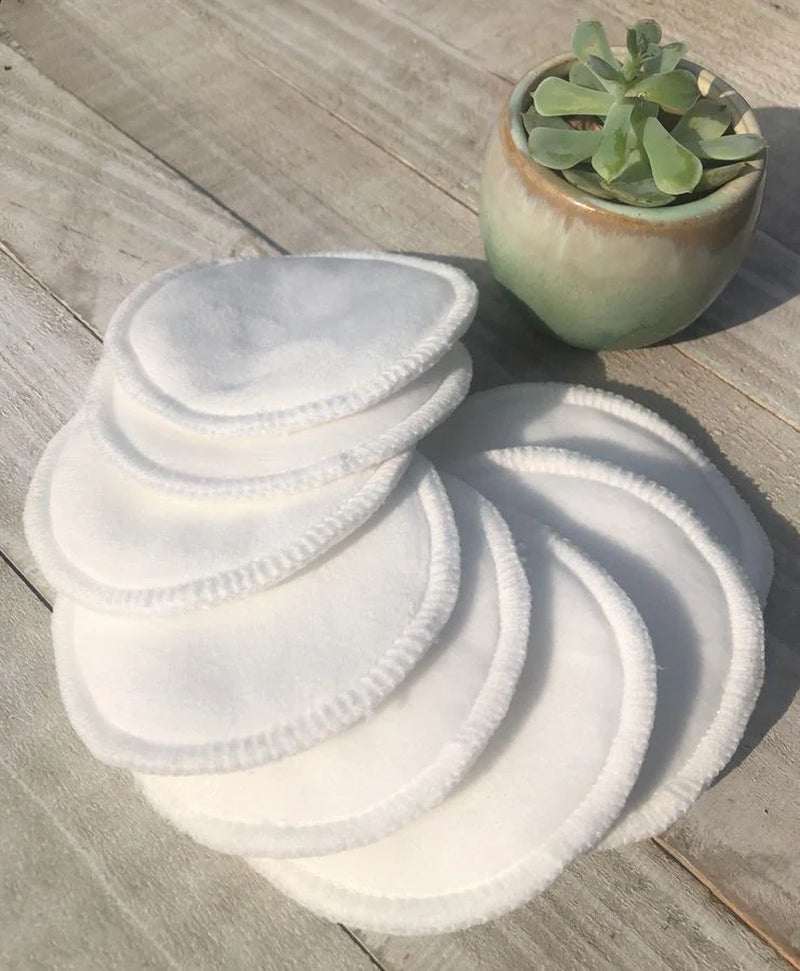 Five reusable eco-friendly facial rounds pads on a wooden surface beside a small plant.