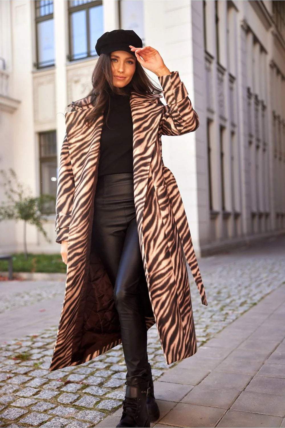 Stylish woman in a zebra print coat and black outfit walking on a city street, showcasing modern fashion.