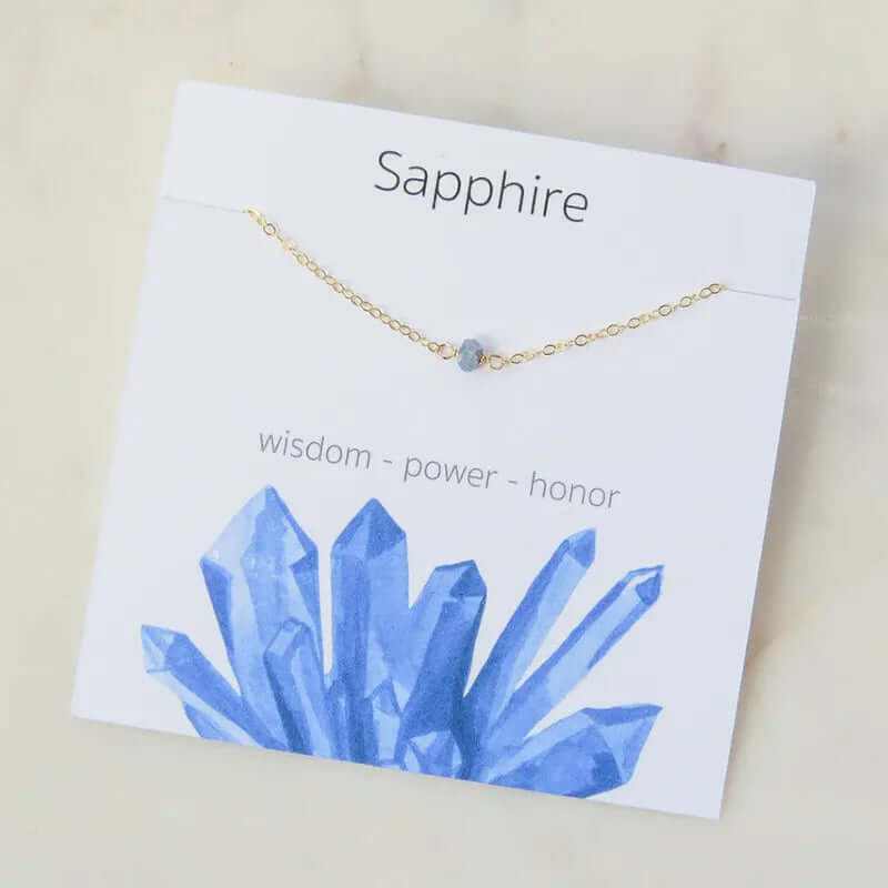 Sapphire charm necklace on a card featuring blue crystal graphics with the words wisdom, power, and honor.
