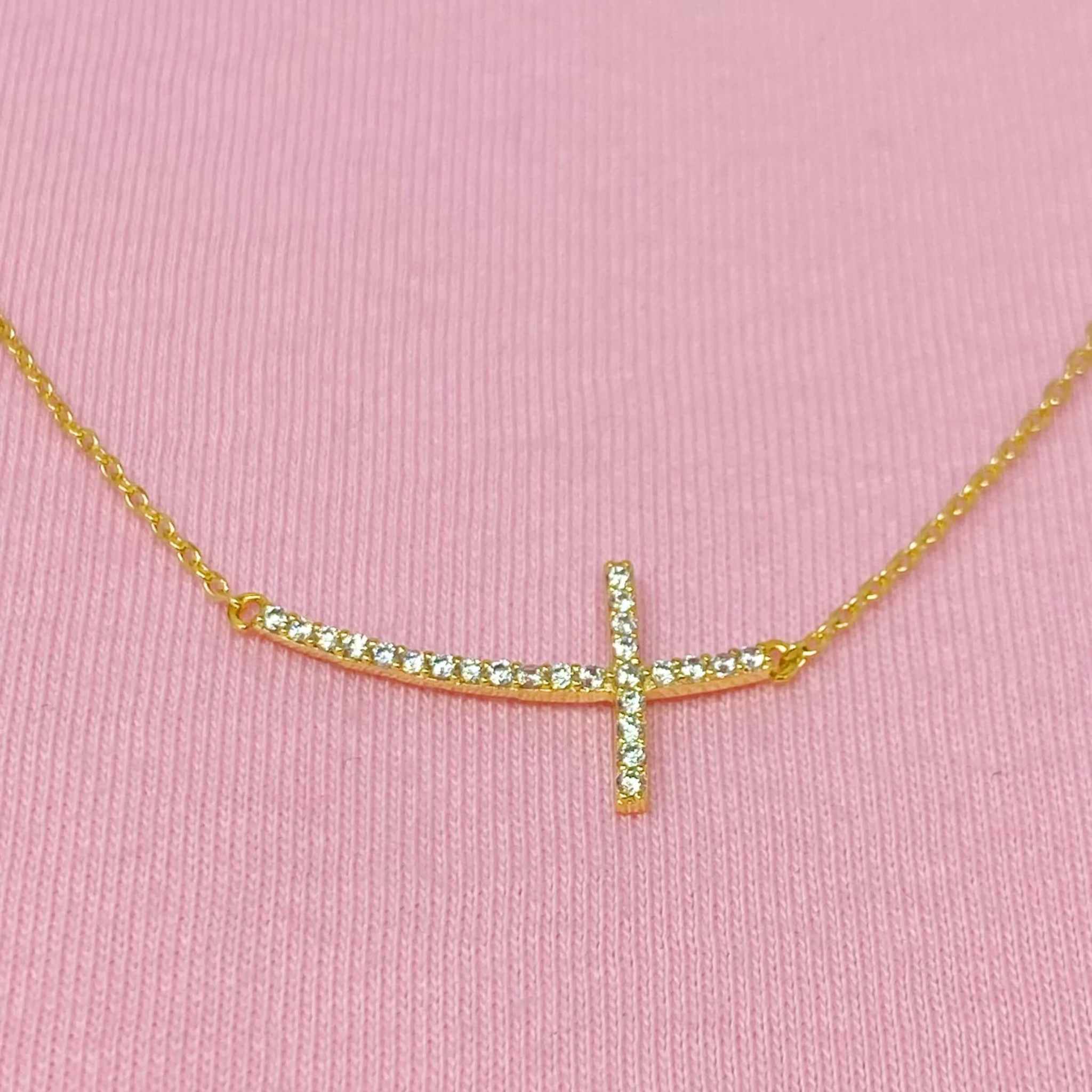 Shiny sideways cross pendant necklace with sparkling gold-plated charm on a delicate chain.