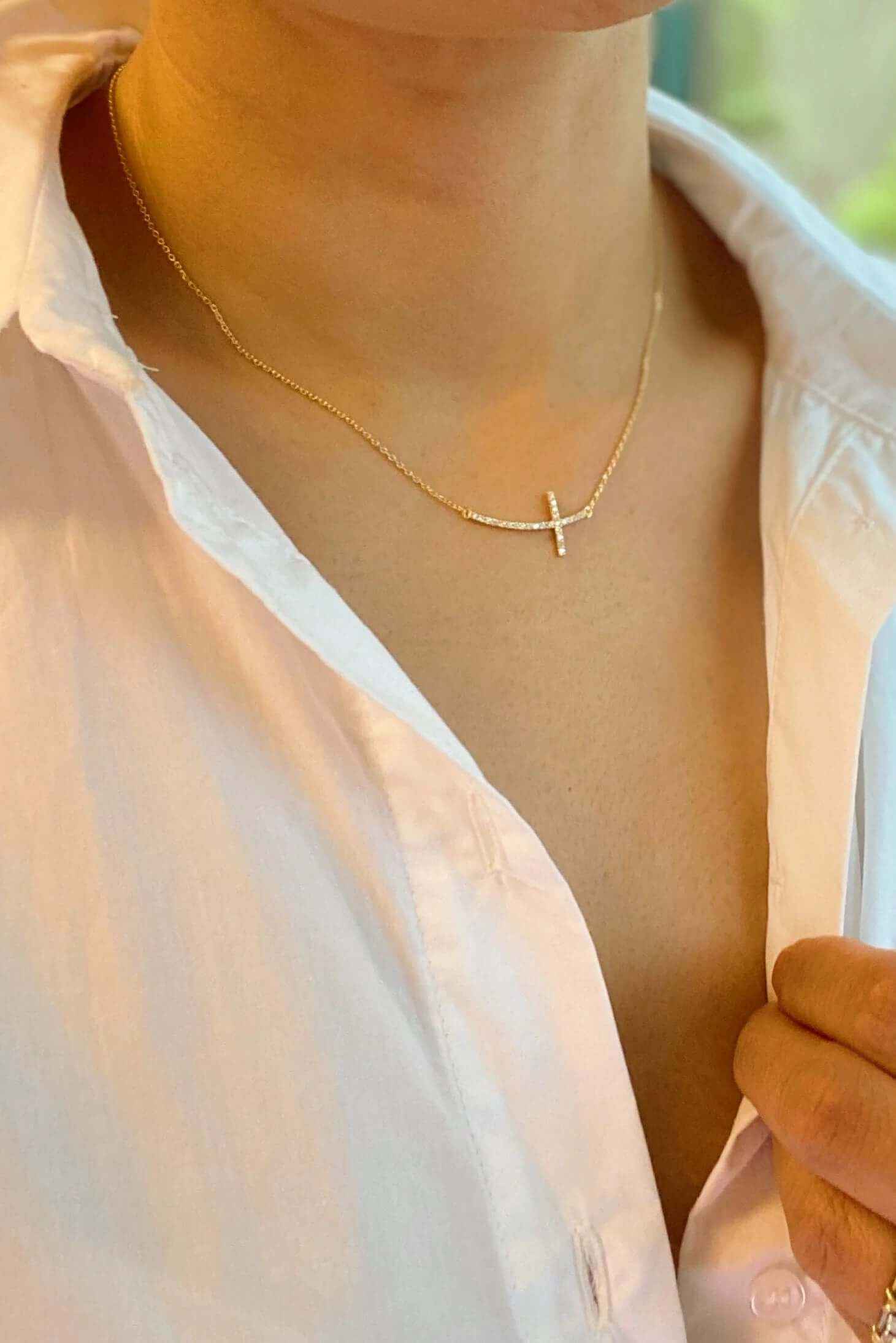 Close-up of a woman wearing a shiny sideways cross pendant necklace with a gold-plated charm.