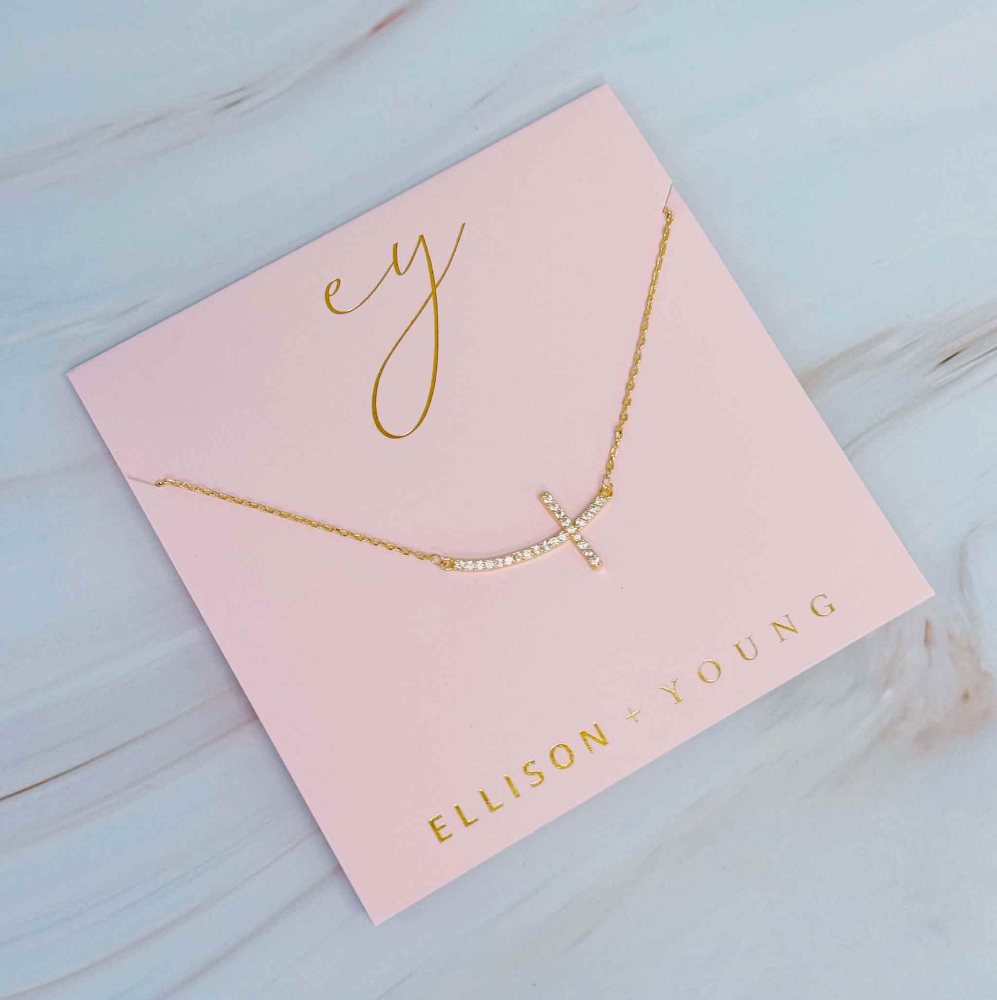Shiny Sideways Cross Pendant Necklace on a pink card by Ellison + Young, elegant and minimalist design.