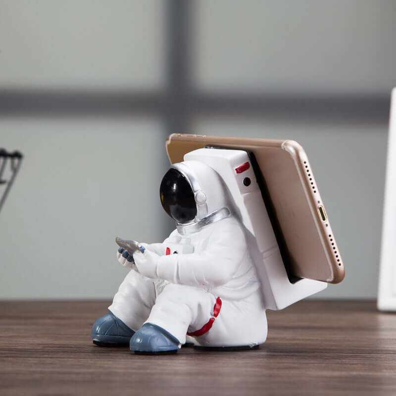 Cute astronaut mobile phone stand on a wooden desk, perfect for students and unique small decorative gift.