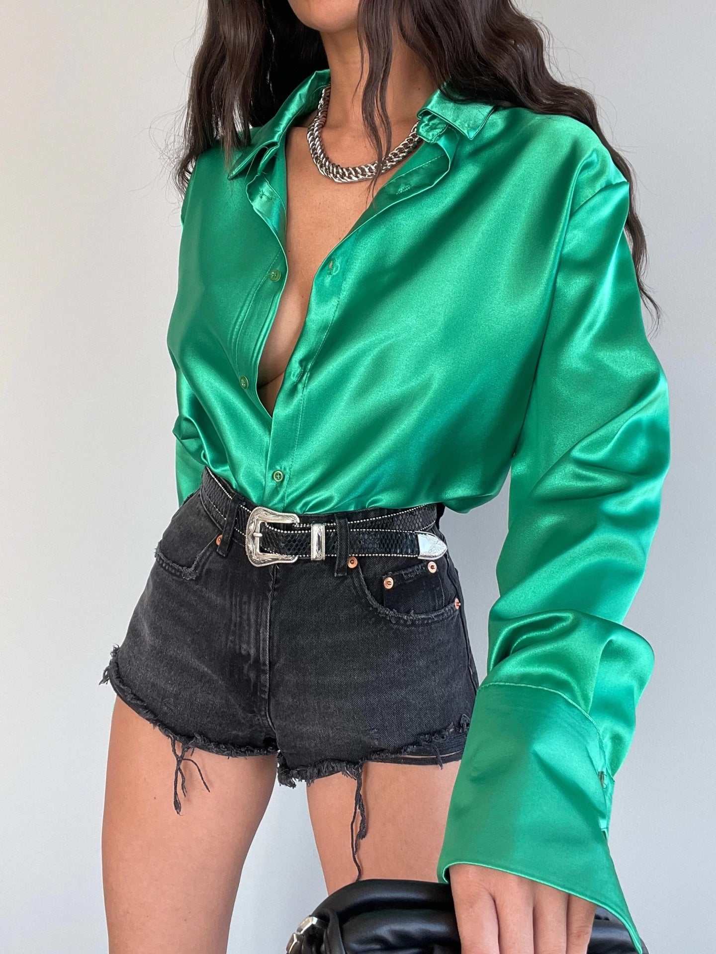 Woman in a green satin long sleeve lapel shirt paired with black denim shorts and accessories.