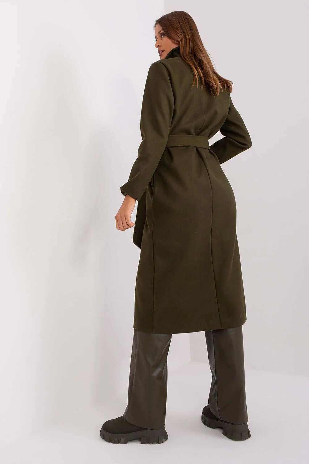 Back view of a stylish mid-length green coat for women with a belt, paired with brown trousers and boots.