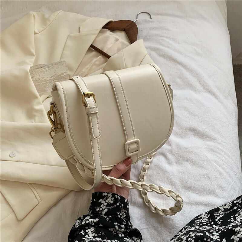 PU stylish trendy women's saddle messenger purse in cream color placed on a white bed with a blazer.