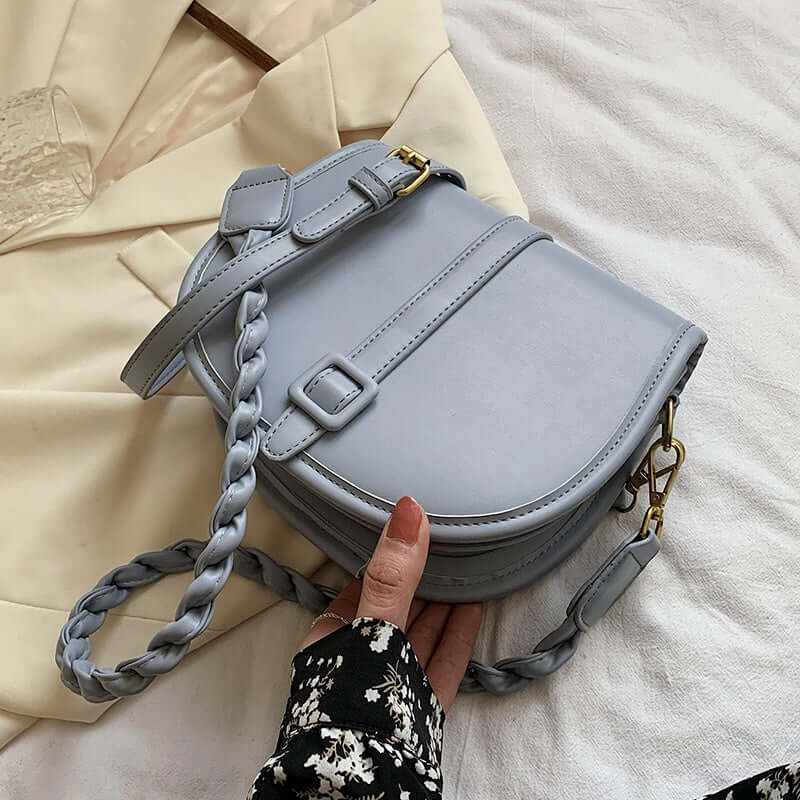 PU stylish trendy women's saddle messenger purse in light blue with braided strap on a stylish background.