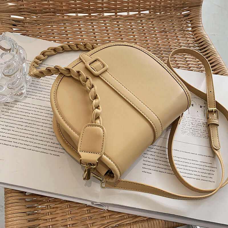 Stylish PU women's saddle messenger purse in beige with braided strap on a woven surface.
