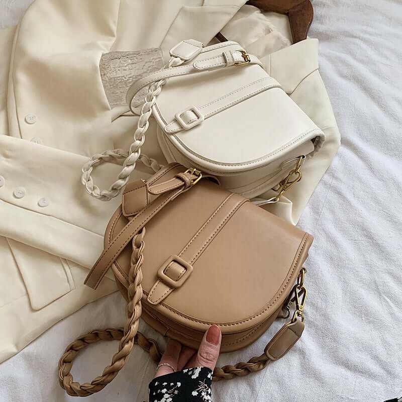 Stylish PU women’s saddle messenger purses in beige and white on a textured surface with a light blazer.