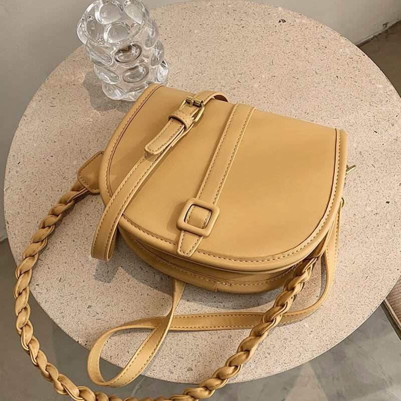 Stylish yellow PU women's saddle messenger purse on a round table with a glass vase.