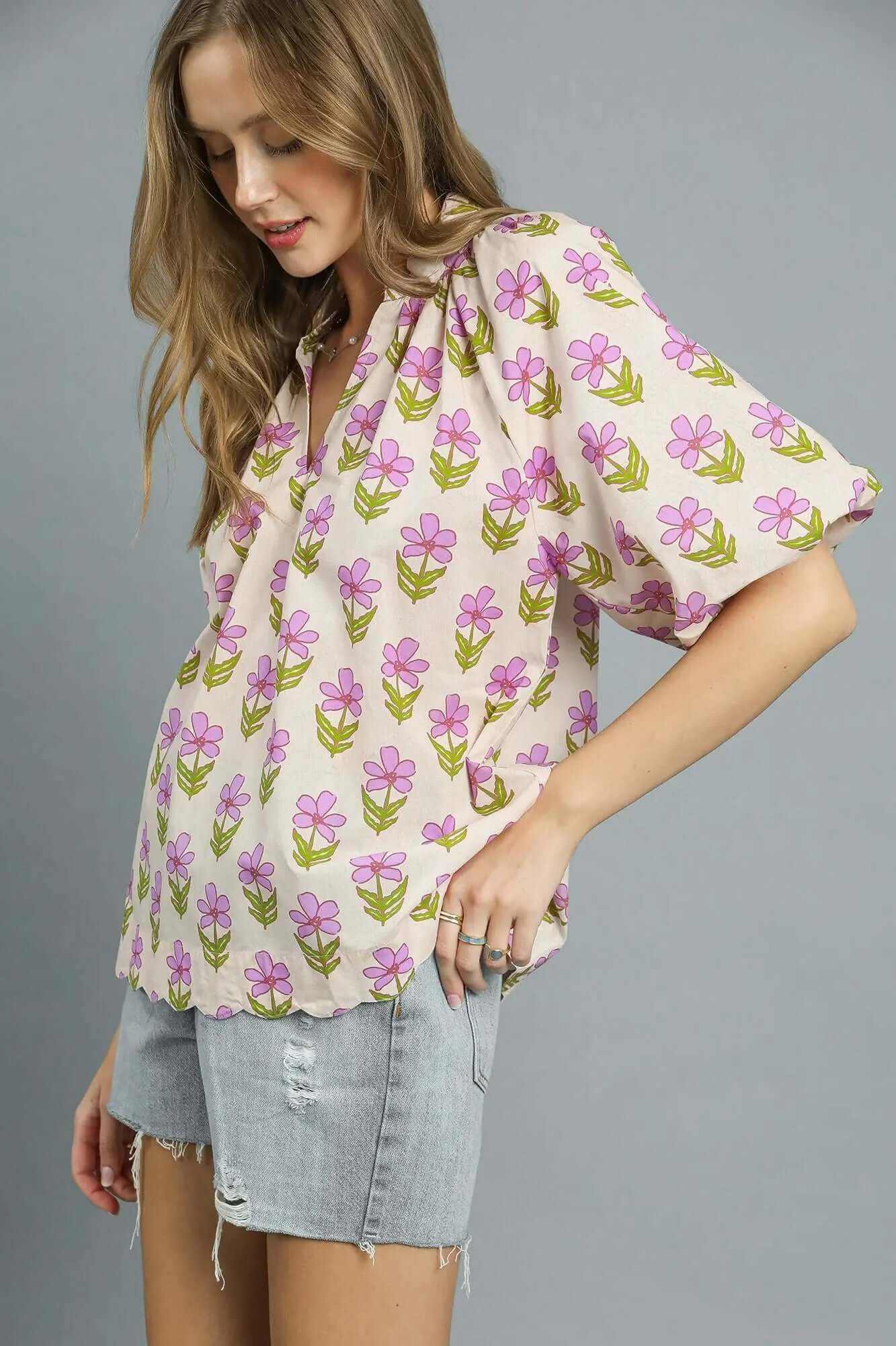 Woman wearing Umgee floral print puff sleeve blouse with pink flowers on a light background, paired with denim shorts.