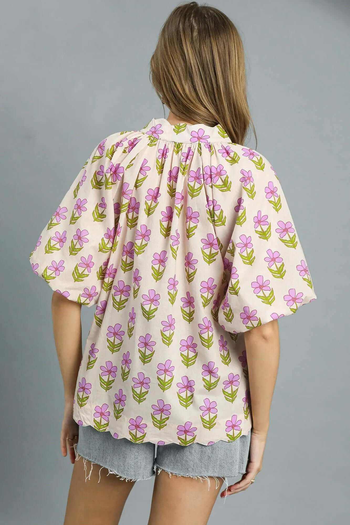 Back view of Umgee floral print puff sleeve blouse in soft pink and green on a light background, paired with denim shorts.