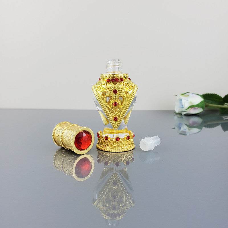 Decorative vintage cosmetic bottle with gold and red gemstone design empty and open with cap on reflective surface