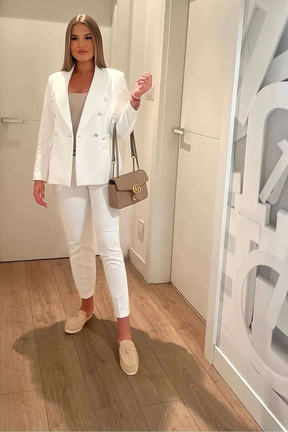 Model wearing a stylish white blazer outfit with matching pants and a handbag, perfect for business or casual settings.