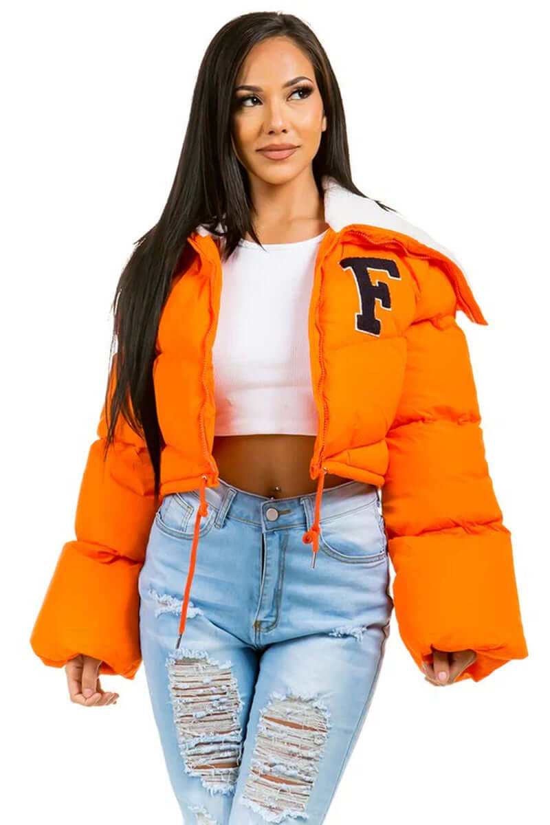 Womens orange puffer jacket with oversized sleeves and letter detail, styled with distressed jeans.