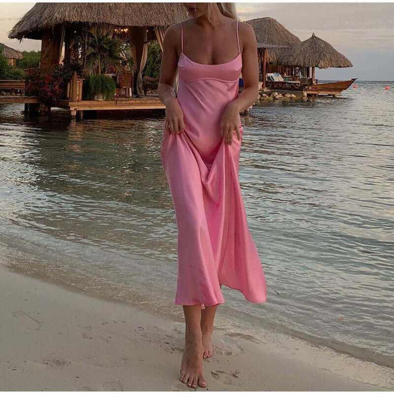 Woman in a pink satin long dress enjoying the beach, showcasing a sleeveless and backless design, perfect for summer.