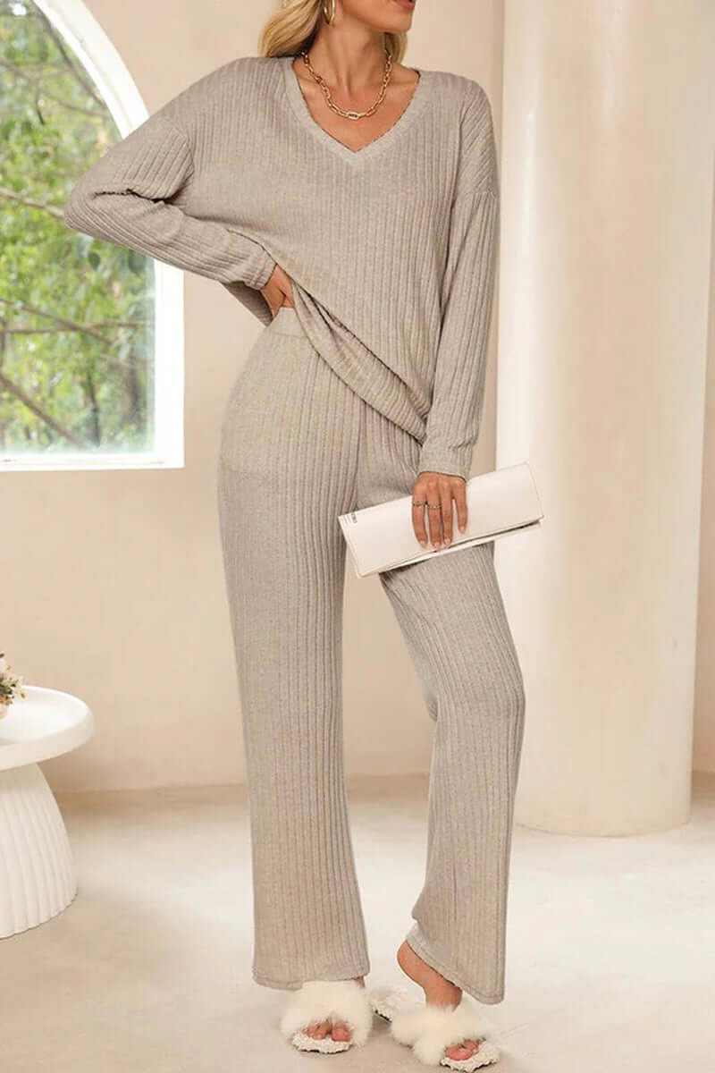 Women wearing a cozy ribbed knit V-neck slouchy two-piece outfit in light gray, styled with a clutch and fluffy slippers.