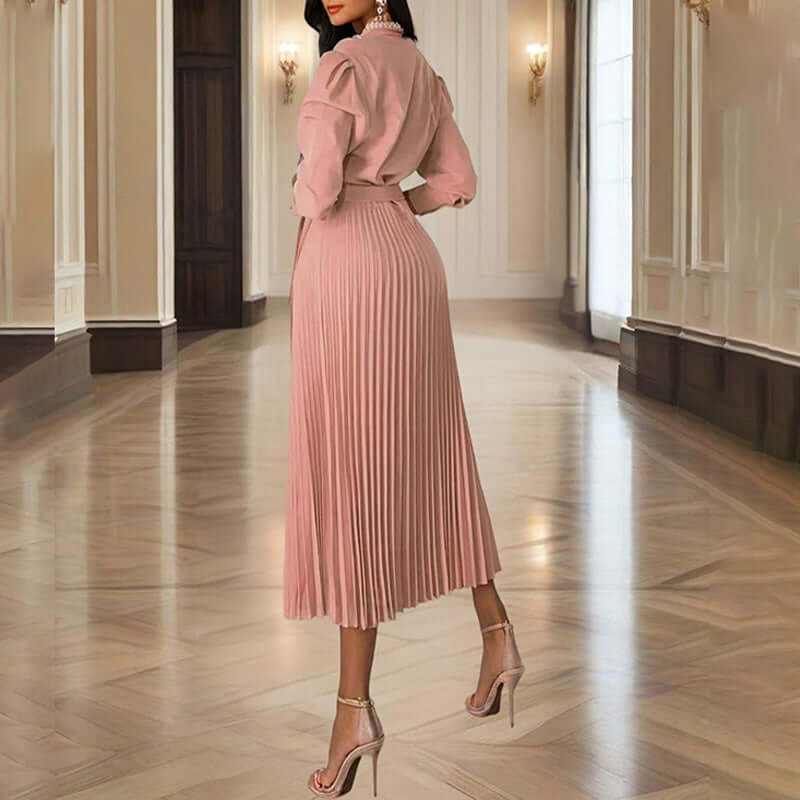 Back view of a woman in a pleated maxi dress with long sleeves, showcasing elegance in a grand interior.