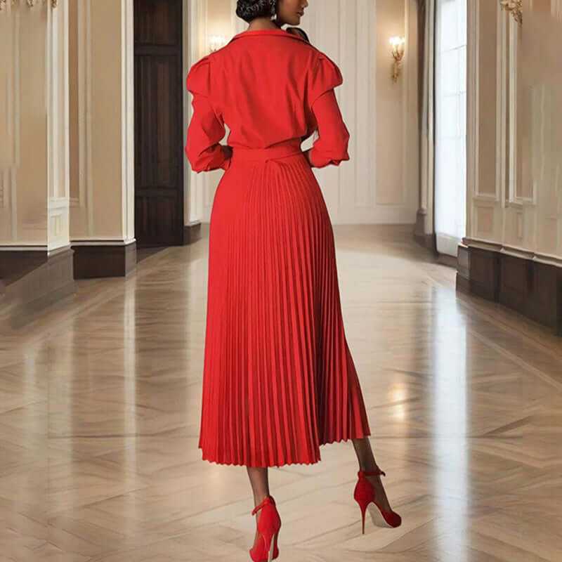 Back view of a woman in a red pleated maxi dress with tie waist, showcasing elegance in a luxurious interior.